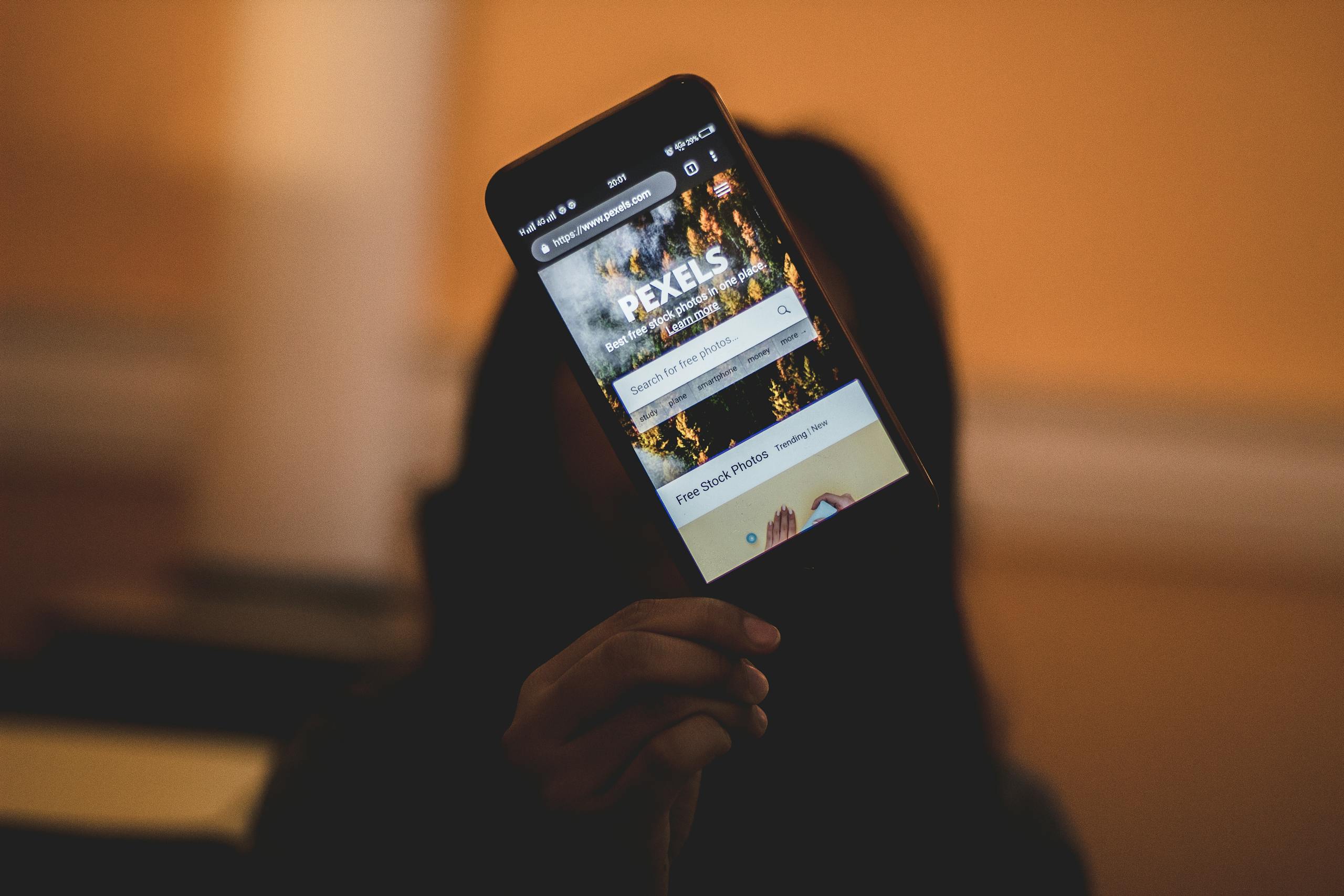 A person holds a smartphone displaying the Pexels website. Ideal for tech and lifestyle themes.